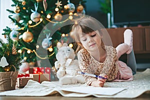 Cute little girl writing a letter near Christmas tree