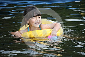 Cute little girl with yellow floaty swimming in the lake