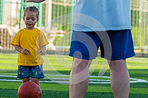 Cute little girl in yellow t-shirt going to kick the ball to father