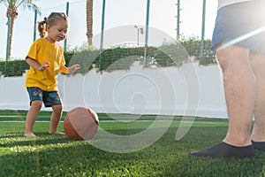 Cute little girl in yellow t-shirt going to kick the ball to father