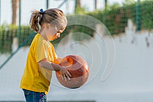 Cute little girl in yellow t-shirt holding ball in her hands and going to kick it