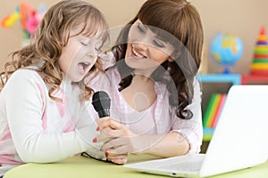 Cute little girl with young mother singing karaoke with laptop at home