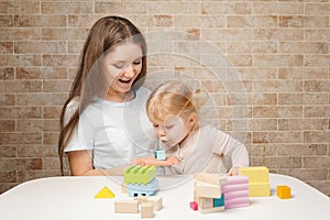 Cute little girl and young mother woman playing with building blocks wooden toys on the table