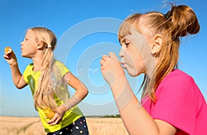 Cute little girls blowing soap bubbles on sunny day