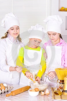 Cute little girls in chef`s hats and aprons preparing dough in the kitchen