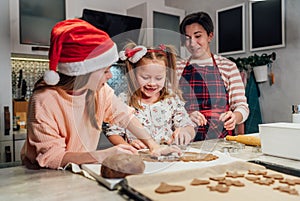 Cute little girls in red Santa hats with mother making homemade dough Christmas gingerbread cookies using cookie cutters together