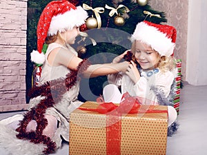 Cute little girls in santa's hat having fun beside a Christmas tree