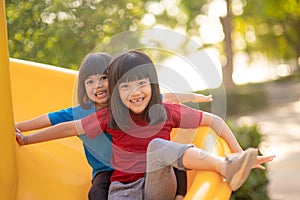 Cute little girls siblings having fun on playground outdoors on sunny summer day. Children on plastic slide. Fun activity for kid