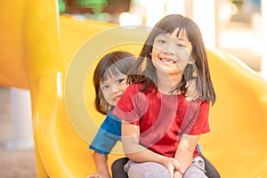 Cute little girls siblings having fun on playground outdoors on sunny summer day. Children on plastic slide. Fun activity for kid