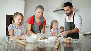 Cute Little Girls and Their Beautiful Parents Knead the Dough and Smile While Cooking in Kitchen at Home.