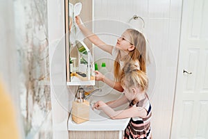 cute little girls washes sink and the bathroom mirror with a special cleaner.