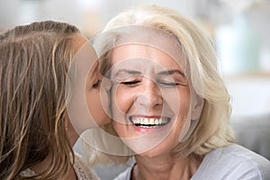 Cute little granddaughter kissing smiling old grandmother on che