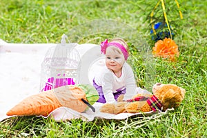 Cute little happy baby girl with big brown teddy bear on green grass meadow, spring or summer season