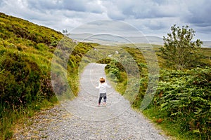 Cute little happy toddler girl running on nature path in Connemara national park in Ireland. Smiling and laughing baby