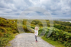 Cute little happy toddler girl running on nature path in Connemara national park in Ireland. Smiling and laughing baby