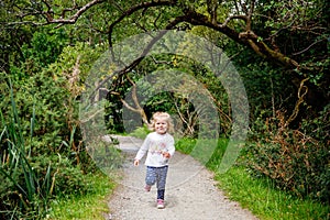 Cute little happy toddler girl running on nature path in Connemara national park in Ireland. Smiling and laughing baby