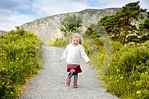 Cute little happy toddler girl running on nature path in Glenveagh national park in Ireland. Smiling and laughing baby
