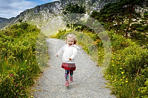 Cute little happy toddler girl running on nature path in Glenveagh national park in Ireland. Smiling and laughing baby