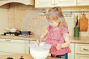 Cute little helper girl helping her mother cooking in a kitchen. Happy loving family are preparing bakery.