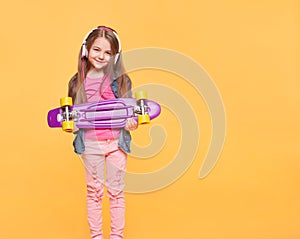 Cute little hipster girl with headphones and skateboard