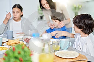 Cute little hispanic boy having breakfast together with his mom and siblings. Latin family enjoying meal together