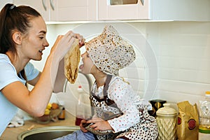 Cute little homecook girl with her beautiful mother makes pancakes in white kitchen