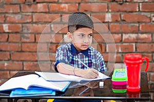 Cute little Indian/Asian school kid studying on study table , writing on notebook with pencil