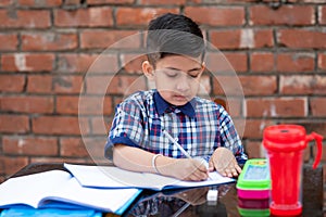 Cute little Indian/Asian school kid studying on study table , writing on notebook with pencil