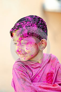 Cute Little Indian boy child with coloured face paint poweder color thrown at his face during holi indian festival looking at