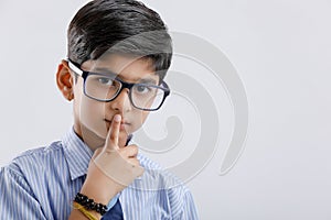 Cute little indian school boy asking / posing to keep silence, standing isolated over white background