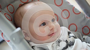 Cute little infant boy sitting in stroller, looking and smiling. Innocence and child emotions