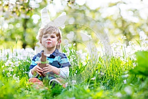 Cute little kid boy with Easter bunny ears celebrating traditional feast. Happy child eating chocolate rabbit fugure on