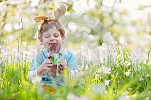 Cute little kid boy with Easter bunny ears celebrating traditional feast. Happy child eating chocolate rabbit fugure