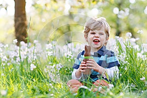 Cute little kid boy with Easter bunny ears celebrating traditional feast. Happy child eating chocolate rabbit fugure