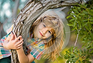 Cute little kid boy enjoying climbing on tree on summer day. Kid happily lying in a tree hugging a big branch.