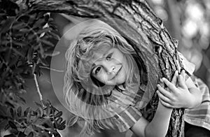 Cute little kid boy enjoying climbing on tree on summer day. Kid happily lying in a tree hugging a big branch.