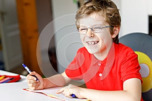 Cute little kid boy with glasses at home making homework, writing letters with colorful pens.