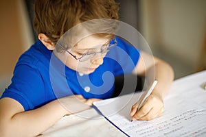 Cute little kid boy with glasses at home making homework, writing letters with colorful pens.