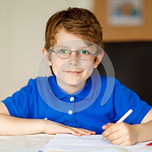 Cute little kid boy with glasses at home making homework, writing letters with colorful pens. Little child doing