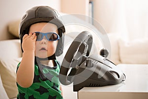 Cute little kid boy in a helmet playing with Computer steering wheel. Future driver. Getting ready for professional driving. Child