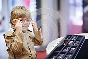 Cute little kid boy at optician store during choosing his new glasses