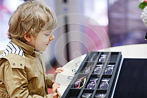 Cute little kid boy at optician store during choosing his new glasses