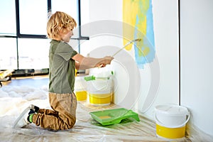 Cute little kid boy painting the wall with color in new house, side view