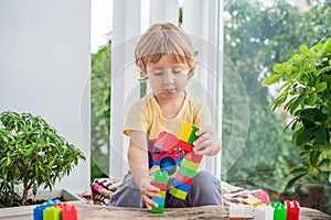 Cute little kid boy with playing with lots of colorful plastic blocks indoor. Active child having fun with building and