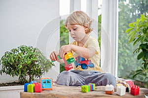 Cute little kid boy with playing with lots of colorful plastic blocks indoor. Active child having fun with building and