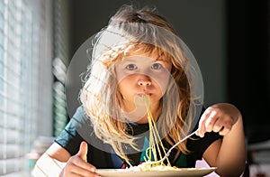 Cute little kid eating spaghetti pasta at home. Close up portrait of funny kid eating. Little boy having breakfast in