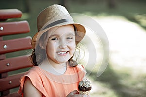 Cute little kid girl in a hat eating ice cream cone. Child sitting on a park bench and laughing . Summer concept