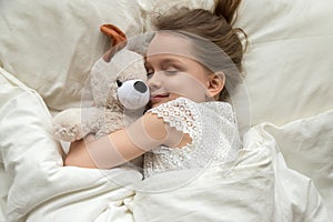 Cute little kid girl hugging teddy bear sleeping in bed