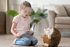 Cute little kid girl playing alone reading book to toy