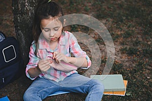 Cute little kid girl, smart primary school student opening her pencil case while doing homework in the park after class